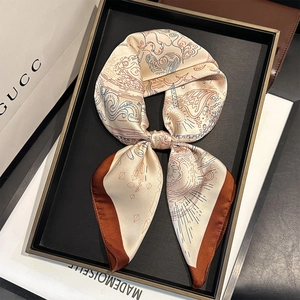 Elegant off-white silk scarf with brown and blue patterns folded in a premium metal tray