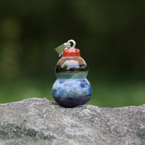 Seven chakra natural gemstone gourd pendant with silver clasp on a grey rock surface