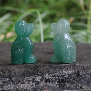Hand-carved green aventurine gemstone puppy figurines on stone surface outdoors