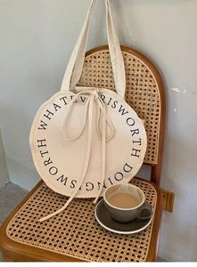 Detail of round cream canvas tote bag with black text hanging on a vintage rattan chair