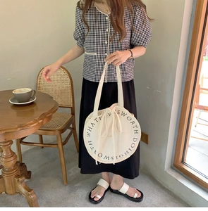 Detail of a minimalist round canvas tote bag with drawstring closure in an aesthetic cafe setting