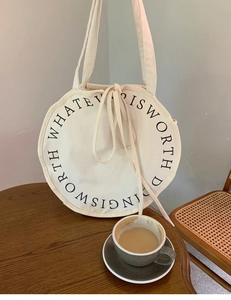 Detail view of round beige canvas shoulder bag with circular typography on a wooden table