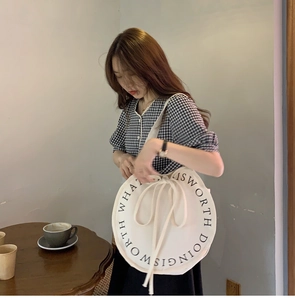 Detail of round canvas shoulder bag featuring a drawstring closure and artistic text print