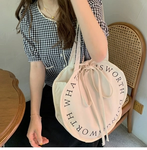 Detailed view of cream round canvas tote bag with black artistic text on woven chair