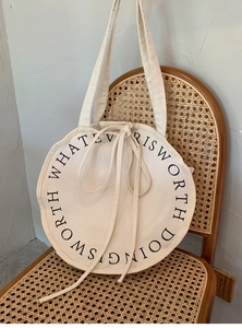 Detail of round canvas bag on vintage chair showing the Whatever Is Worth Doing print