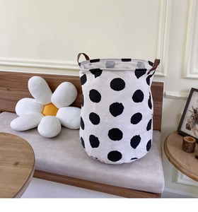 Detail of canvas laundry basket with black polka dots and brown leather handles