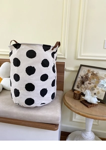 Close-up of foldable canvas laundry basket featuring black polka dots and leather handles