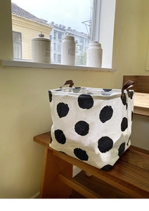 Polka dot canvas laundry basket with premium leather handles on a rustic wooden bench