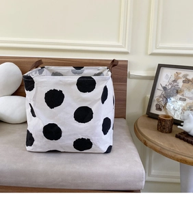Close-up of a white polka dot canvas laundry basket with brown leather handles in a cozy room