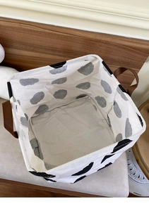 Close-up of foldable fabric storage bin with cow print pattern and leather handles