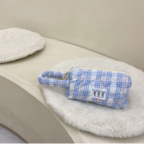 Detailed shot of a quilted blue gingham toiletry bag with daisy zipper and floral patch