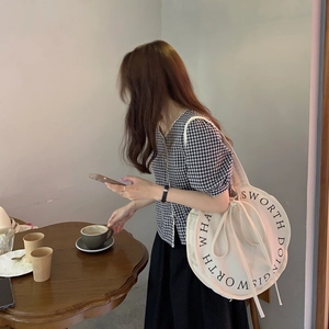 Minimalist round canvas shoulder bag with letter print and drawstring in a cafe setting