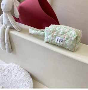 Detail of green quilted plaid makeup bag with floral patch and soft handle grip