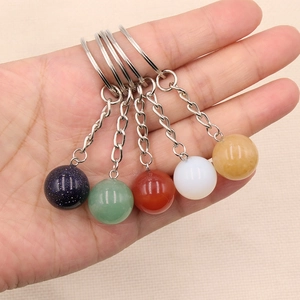 Hand holding 16mm natural crystal ball keychains in assorted healing gemstones