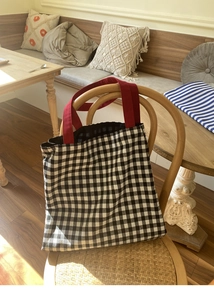 Détail du sac cabas en toile vichy avec poignées rouges sur une chaise en bois