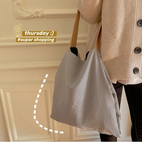Détail du sac cabas en toile rayée avec anses en cuir porté par un mannequin