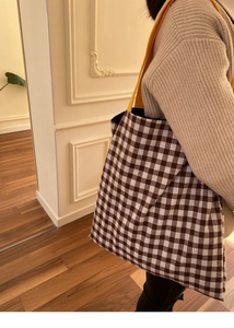 Détail d'un sac cabas à carreaux avec anses jaunes porté par un mannequin en pull