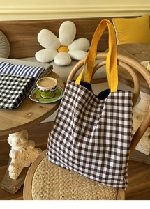 Détail du sac cabas en toile à carreaux avec anses jaunes sur une chaise en bois