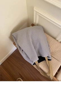 Détail d'un sac cabas en toile rayée avec anses kaki posé sur un banc tressé
