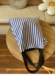 Détail du sac cabas en toile à rayures bleues et blanches sur une table en bois clair