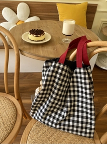 Vue détaillée d'un sac cabas en toile vichy noir et blanc avec anses rouges sur une chaise