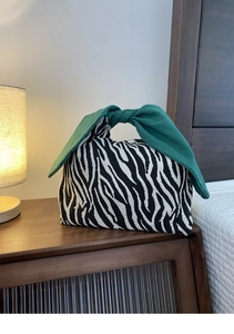 Dettaglio di borsa zebrata con grande manico a fiocco verde scuro su un comodino in legno