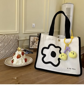 Détail du sac cabas en toile blanche avec liseré noir, imprimé floral et breloque cerise