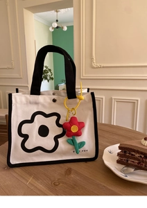 Détail du sac à lunch en toile avec motif floral noir et breloque tournesol sur table