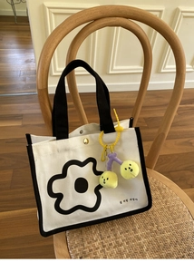 Détail du sac cabas en toile avec imprimé floral, anses noires et breloque cerise