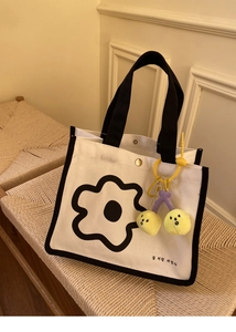 Détail d'un sac en toile blanc avec imprimé fleur noire et pendentif cerise jaune