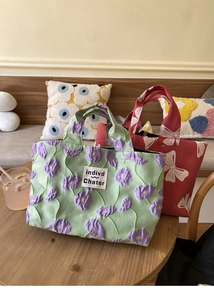 Detailed shot of bow knot textured tote bags in mint green and red on a wooden desk