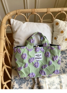 Close-up of light green tote bag with purple floral jacquard and brand label on a chair