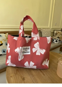 Close-up of red canvas tote bag with white bow pattern and brand label on a wooden table