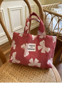 Detail of red fabric handbag featuring white bow patterns and indivd Chater woven label