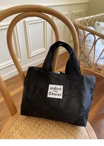 Detail of black bow textured handbag with brand label on a vintage woven chair
