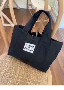 Close-up of black tote bag with embroidered 3D bows on a wooden wicker chair