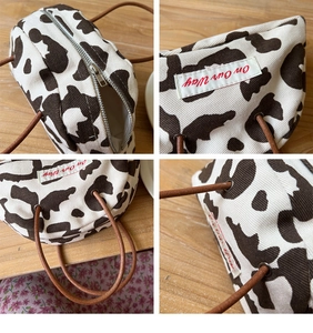 Detailed close-up of cow print canvas handbag showing silver zipper and logo patch