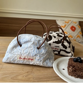 Close-up of semi-circular denim handbag with floral and cow print patterns on a table