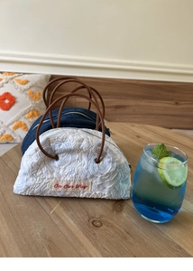 Detail of denim and jacquard semicircular handbags with On Our Way red label on wood