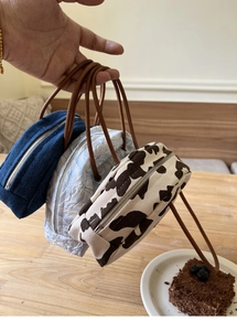 Three semi-circle denim and cow print handbags with rope handles and zippers on a table