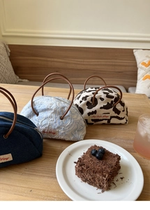Three semi-circular denim and cow print tote bags displayed in a cozy cafe setting