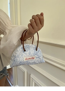 Detail of blue floral embossed denim handbag with On Our Way tag and brown handles