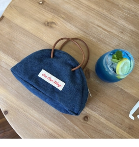 Macro detail of dark blue denim handbag with white label and brown leather handles