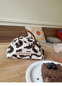 Detail of a mini cow print canvas bag with brown leather handles and 'On Our Way' embroidery