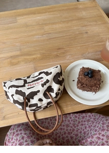 Detail of cow print canvas bag with round brown handles on a wooden table setting