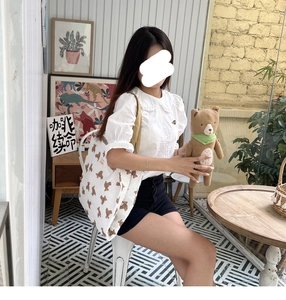 Close-up of a cream canvas tote bag featuring brown cartoon bear prints and khaki straps