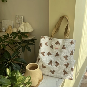Detail of bear pattern on quilted beige tote bag with woven khaki handles and brand label