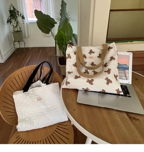 Detail of quilted white tote and teddy bear print shoulder bag on a wooden table