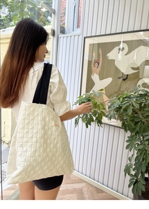 Quilted white tote bag with black straps and red logo detail shown on a model