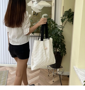 Detail of white quilted tote bag featuring a grid texture and comfortable wide black strap
